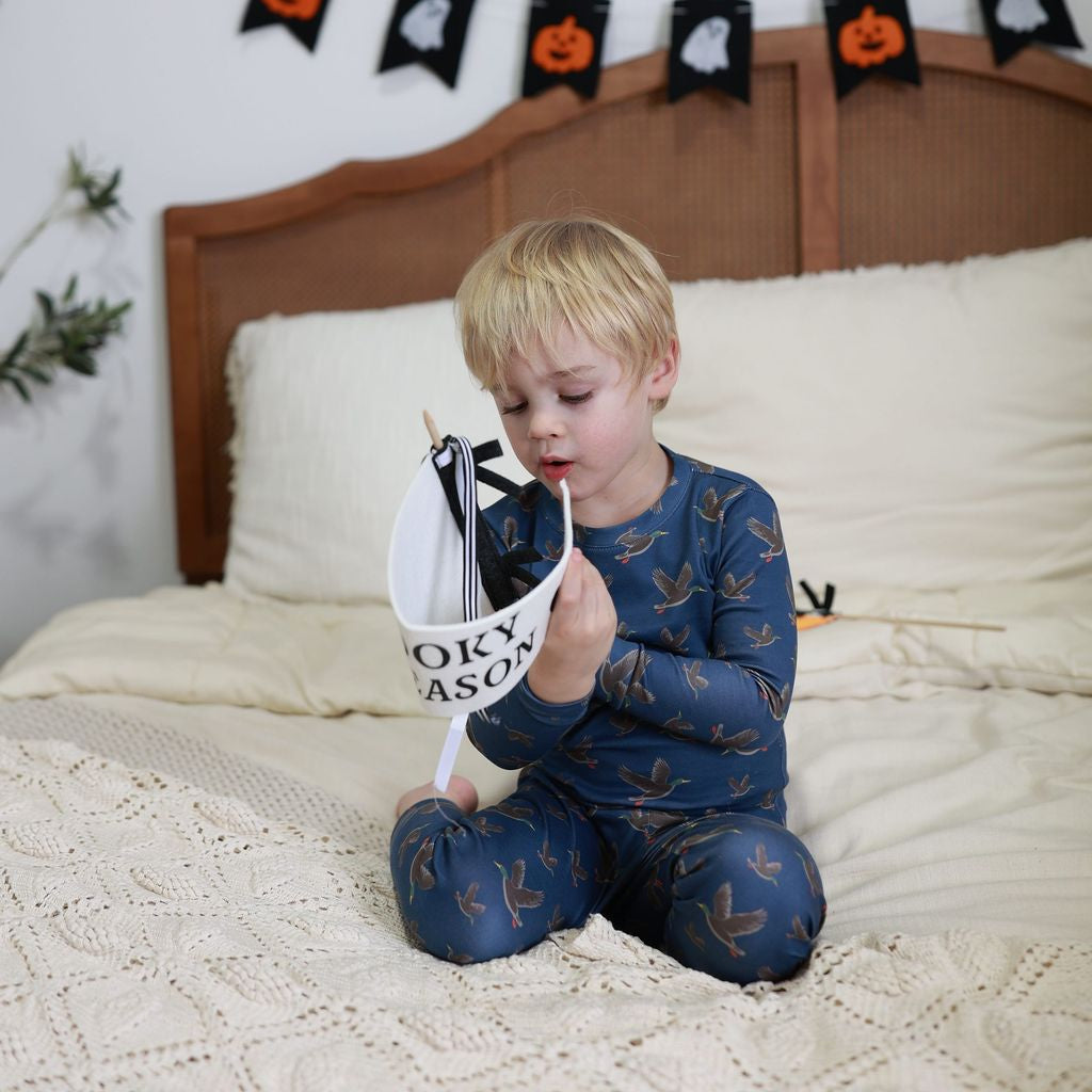 Child sitting on a bed holding a Halloween-themed bag with decorations on the wall.