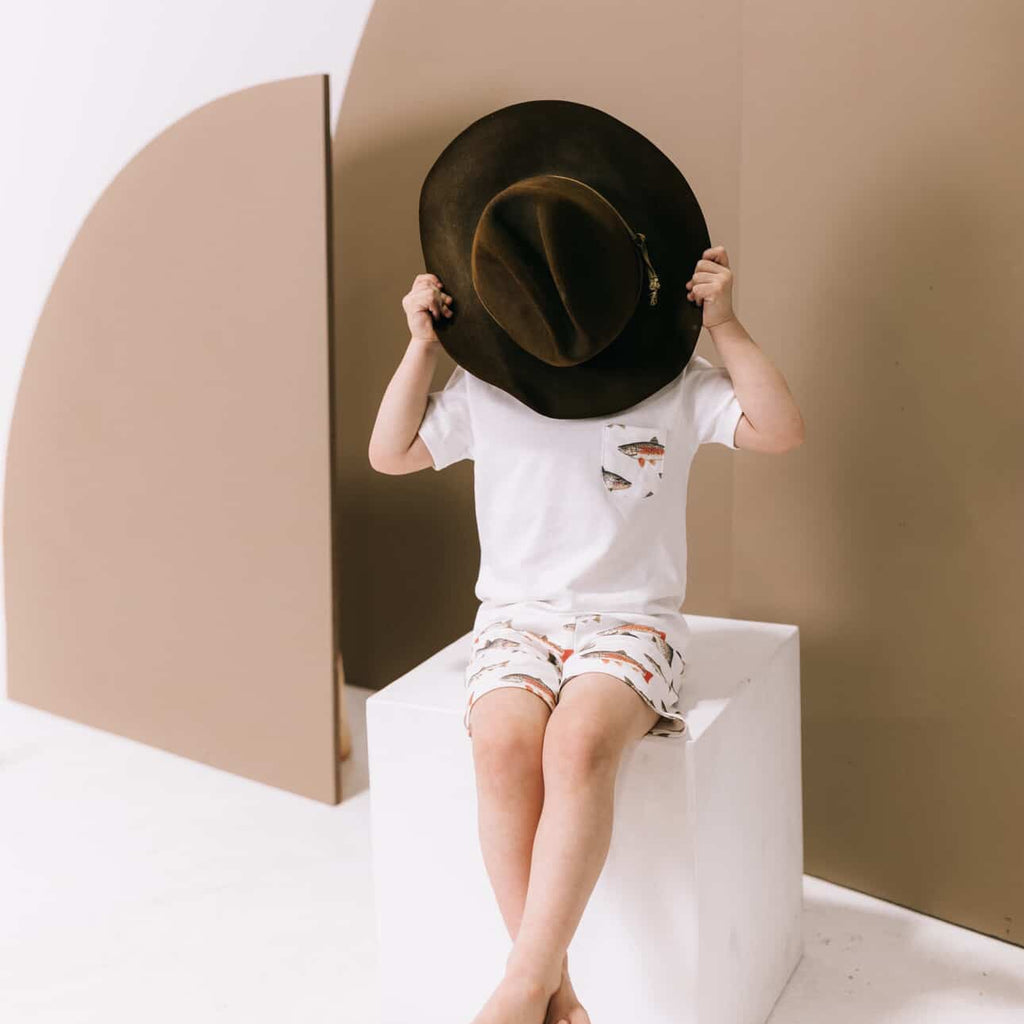 Child playing with a large black hat in a minimalistic setting with geometric shapes.